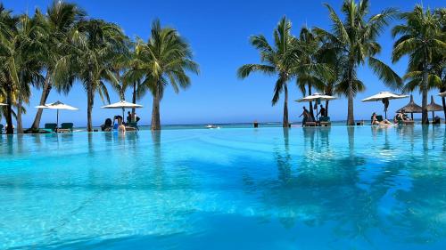 a swimming pool with palm trees and people sitting on the beach at PAILLE EN QUEUE with HEATED POOL PISCINE CHAUFFEE in Rivière Noire