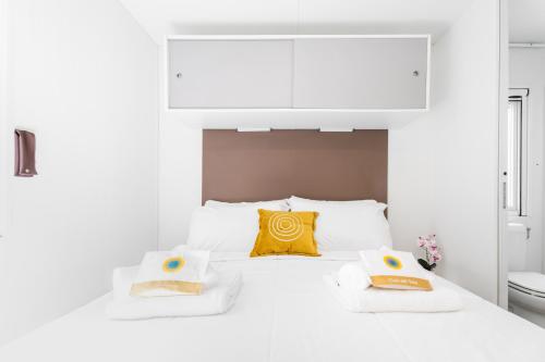 a white bedroom with a white bed with a yellow pillow at Club del Sole Vigna sul Mar Family Collection in Lido di Pomposa