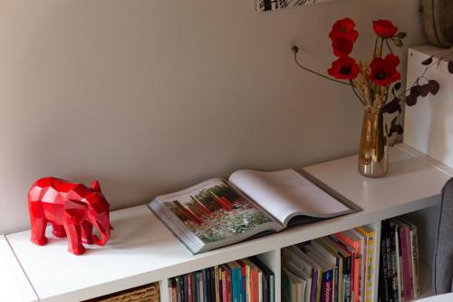 a shelf with a book and a vase with red roses at Charmant Appart, terrasse verdoyante, proche Paris in Saint-Maur-des-Fossés