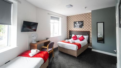 a bedroom with two beds with red pillows and a desk at Imperial Salford Hotel in Manchester