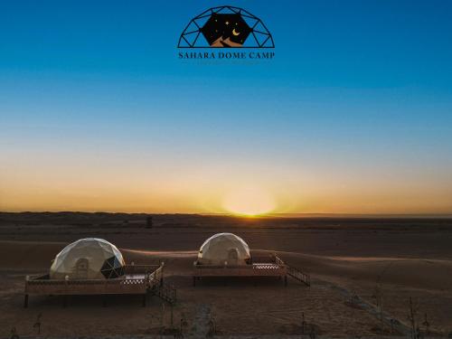 two tents in the desert with the sunset in the background at Royal Sahara Dome Camp in Merzouga