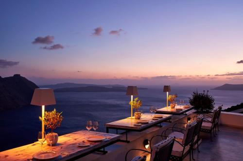 a group of tables on a balcony with a view of the ocean at San Antonio - Small Luxury Hotels of the World in Imerovigli