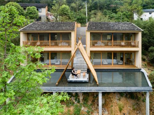 a house with a person sitting on a table in front of it at 大山初里 Origin Villa Village Hotel&Resort in Tonglu