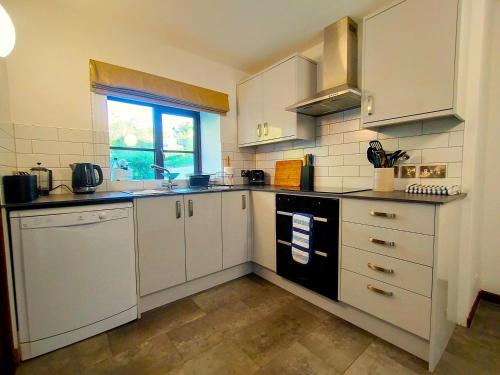 a small kitchen with white cabinets and a window at The Long Barn for Families Walker Pets & Workers in Penzance