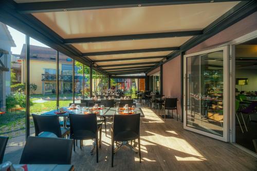 a restaurant with tables and chairs and windows at Résidence Les Rives de la Fecht - Colmar Ouest in Ingersheim