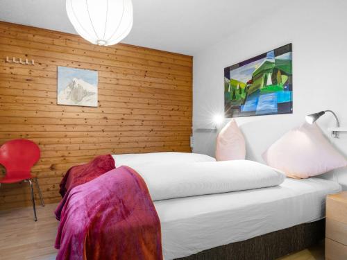 a bedroom with a white bed and a wooden wall at Chalet Rietsli by Interhome in Grächen