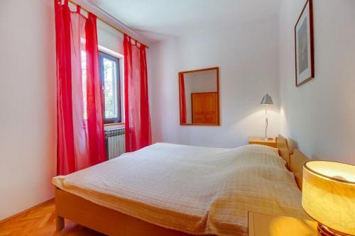 1 dormitorio con 1 cama con cortinas rojas y ventana en Apartments Eli, en Mali Lošinj