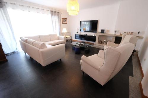 a living room with white chairs and a tv at high standard rental in a quality residence with pool, tennis and view of the ocean in antas esposende 12 people in Esposende