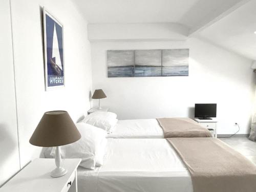 - une chambre blanche avec 2 lits et une lampe dans l'établissement Beach Nest, à Hyères