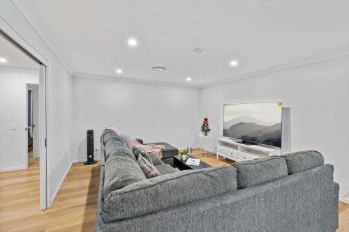 a living room with a gray couch and a flat screen tv at Stunning 5BR Big Modern Home with Parking Malls and Parks in Brisbane