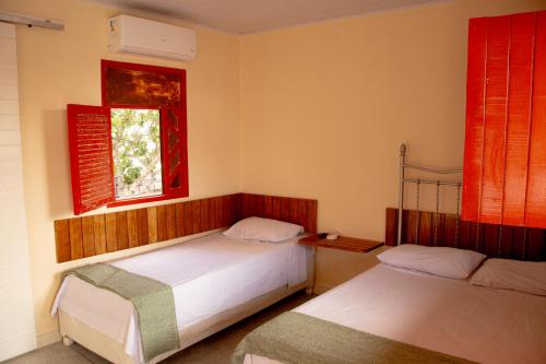 a bedroom with two beds and a window with red shutters at Pousada Umbuzeiro in Piranhas