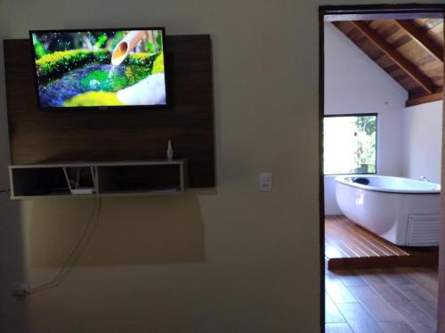 a bathroom with a tub and a tv on the wall at Chalé Portal Lazer Propriedade Inteira in Gonçalves