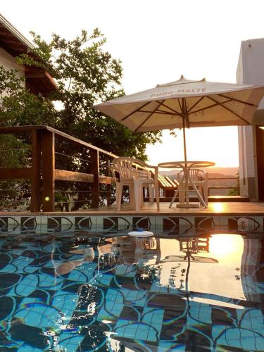 a swimming pool with an umbrella and chairs at Villa Macacos in Nova Lima