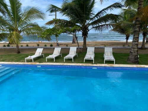 a pool with chairs and palm trees next to the beach at The Palm Bay Club Lodge in Nagua