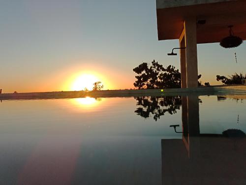 a sunset over a swimming pool with the sun setting at Villa Queridoro Mahahual in Mahahual