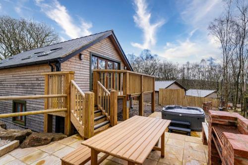 a log cabin with a grill and a wooden deck at Derwent, woodland lodge with hot tub for 6 in Oakamoor