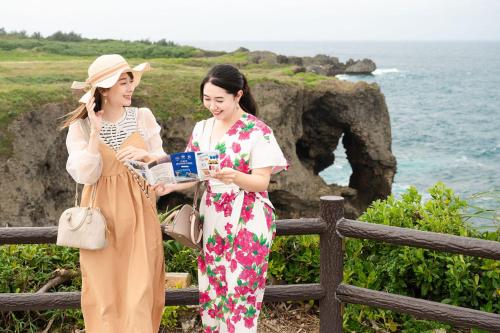two women standing next to a fence looking at a book at 美らVacation in Onna