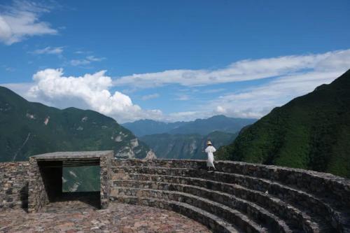 a person standing on a stone wall looking at the mountains at MUUA Hotel in Wushan