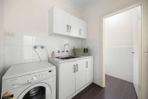 a white kitchen with a washing machine and a sink at Mawson Lakes Retreat - 3BR, Wifi, Parking in Mawson Lakes