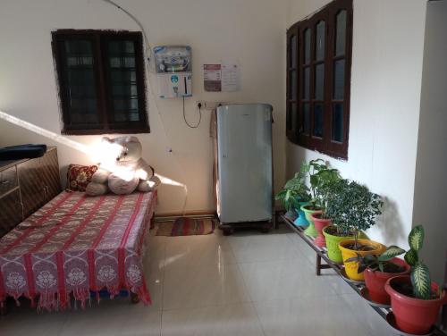a room with a bed and potted plants and a refrigerator at Aarti Home Stay Tapovan in Tapovan