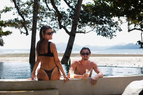 a man and woman in bikinis sitting on a wall in the water at Parada Beach Camp in El Nido
