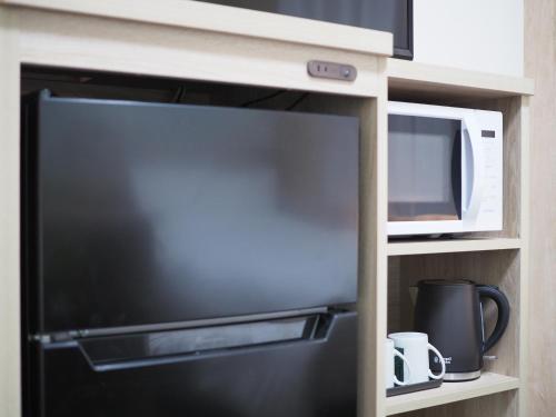 a microwave and a black refrigerator in a kitchen at Tabino Hotel EXpress Narita in Narita