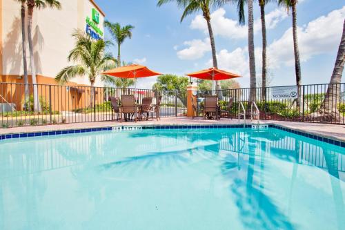 a swimming pool with chairs and umbrellas and palm trees at Holiday Inn Express and Suites Fort Lauderdale Airport West by IHG in Davie