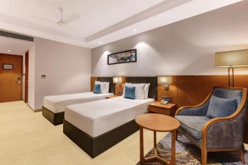 a hotel room with two beds and a chair at Lemon Tree Premier, Dwarka in Dwarka