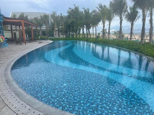 a large blue swimming pool with palm trees in the background at Ho Tram Beach House in Xuyên Mộc