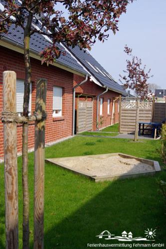 a house with a yard with a tree and a fence at 01 Sommerhus Esbjerg DHH mit Sauna und Whirlpool in Burg auf Fehmarn