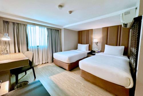 a hotel room with two beds and a desk at Ramada Sukhumvit Soi Eleven in Bangkok