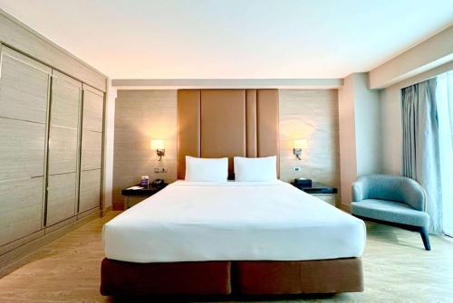 a bedroom with a large white bed and a blue chair at Ramada Sukhumvit Soi Eleven in Bangkok