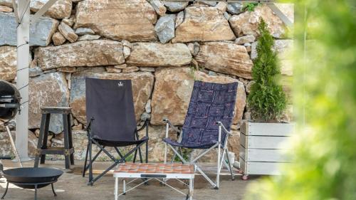 two chairs and a table in front of a stone wall at Gapyeong Dongban84 Glamping&Pool villa in Gapyeong