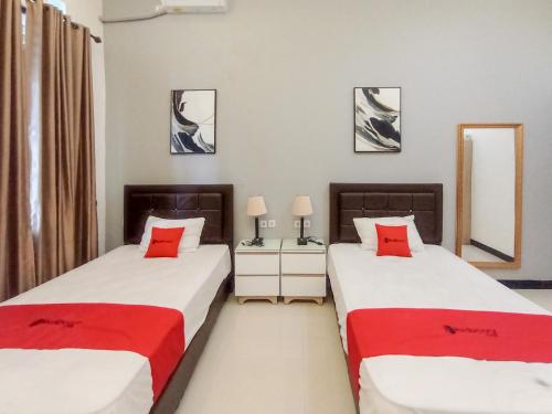 two beds in a room with two red pillows at RedDoorz at Wisma Garden Purwokerto in Purwokerto