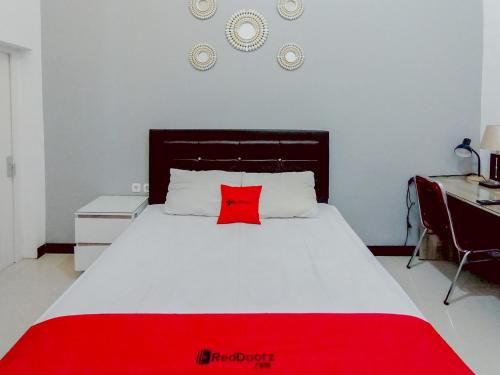 a bedroom with a red pillow on a white bed at RedDoorz at Wisma Garden Purwokerto in Purwokerto