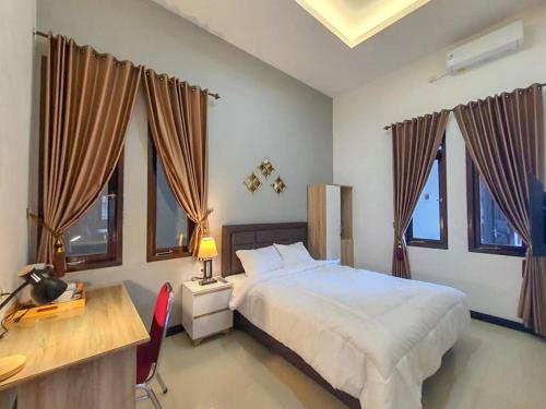 a bedroom with a bed and a desk and windows at RedDoorz at Wisma Garden Purwokerto in Purwokerto