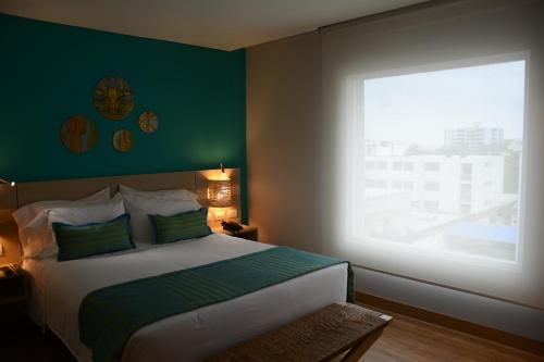 a bedroom with a bed with a green wall and a window at bh Barranquilla in Barranquilla