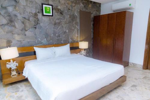 a bedroom with a white bed and a stone wall at FLAMIGO ĐẠI LẢI RESORT - Villa View Hồ in Ngọc Quang