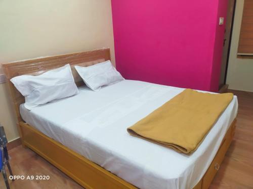 a bedroom with a white bed with a pink wall at Manasa Inn in Palakkad