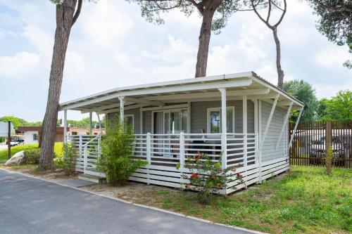 a small white house with a porch and trees at Club del Sole Adriano Family Collection in Punta Marina