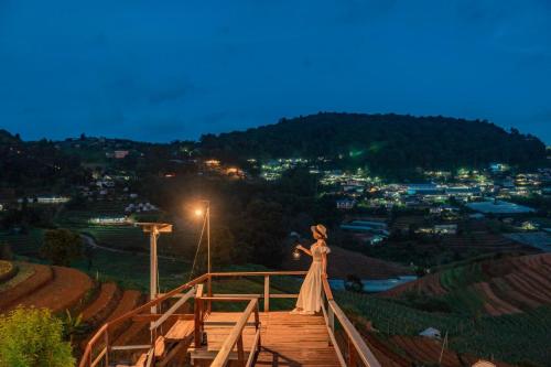 a woman in a dress standing on a wooden bridge at ไร่อมรพญา ม่อนแจ่ม เชียงใหม่ in Mae Rim