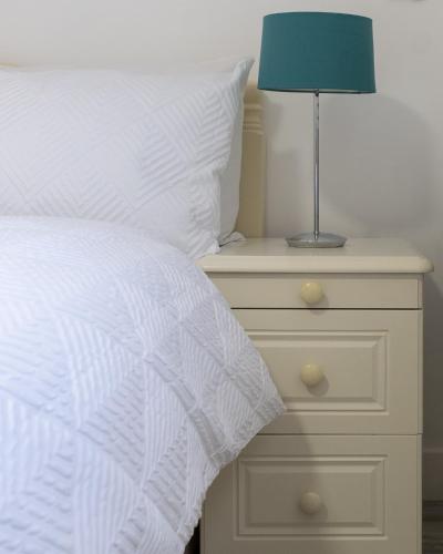 a bed with a white comforter and a lamp on a night stand at Oak Lodge in Welling