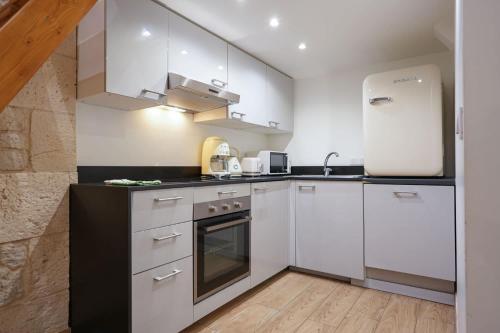 La cuisine est équipée de placards blancs et d'un réfrigérateur noir et blanc. dans l'établissement Loft 2 BR Marais, Notre Dame AC by LCC Agency, à Paris