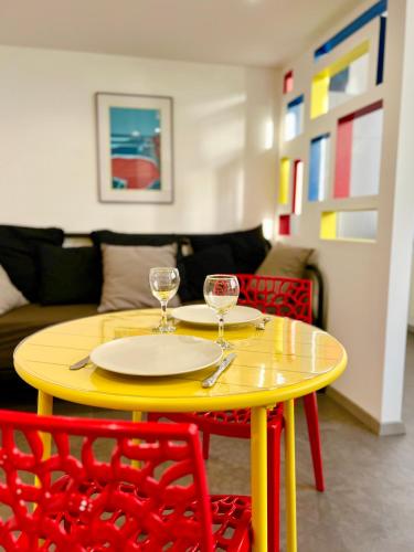 une table jaune avec deux verres à vin et des chaises rouges dans l'établissement L'Atypique, Confort, Centre-ville, à Royan