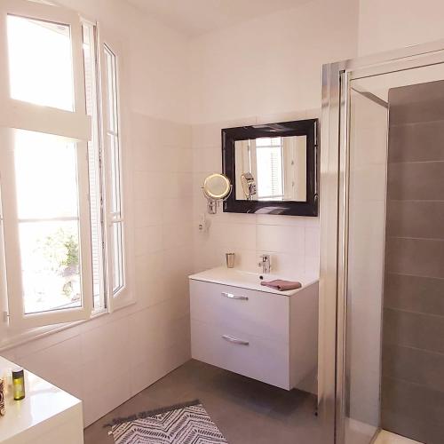 une salle de bain blanche avec un lavabo et un miroir dans l'établissement Bel F2 près de la plage, à Ajaccio