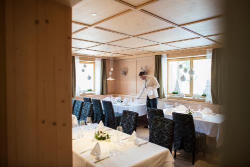 a woman standing in a dining room with tables and chairs at Biancaneve Family Hotel in Selva di Val Gardena