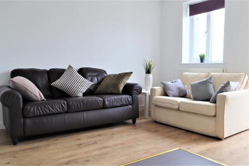 sala de estar con sofá de cuero negro y sofá blanco en Heron House, en Thrapston