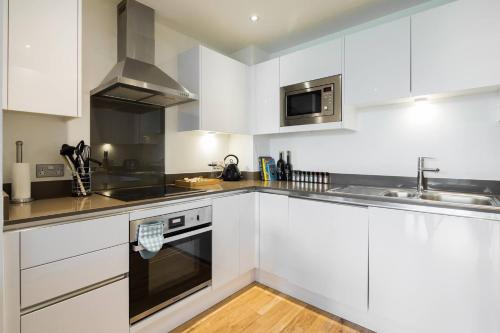 a kitchen with white cabinets and a sink and a stove at Wild Roses Serviced Apartments - Greenwich in London