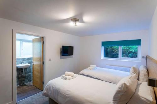 a bedroom with two beds and a bathroom with a sink at Errwood, woodland lodge with hot tubs for 14 in Oakamoor