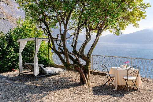 a table and chairs under a tree next to the water at Hotel Royal Victoria, by R Collection Hotels in Varenna